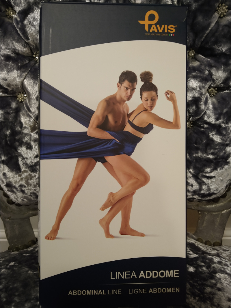 The cardboard box that the truss came in is propped up on a chair. The word 'Pavis' is at the top, with 'Linea Addome', 'Abdominal Line' and 'Ligne Abdomen' underneath. In the centre is a muscular man in purple underwear holding a woman also in purple underwear from behind. Her hair is in a bun and she is poised on one foot, on tiptoe, apparently being kept from falling over by a long length of purple silk cloth attached off camera on the left hand side. The man's hand is buried in the cloth. He looks deeply concerned, or angry. The woman has her right arm raised and is looking down at the man's hand.